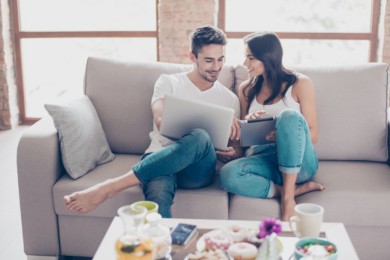 Jovem casal feliz sentado no sofá fazendo compras online no notebook com cartão de crédito. 