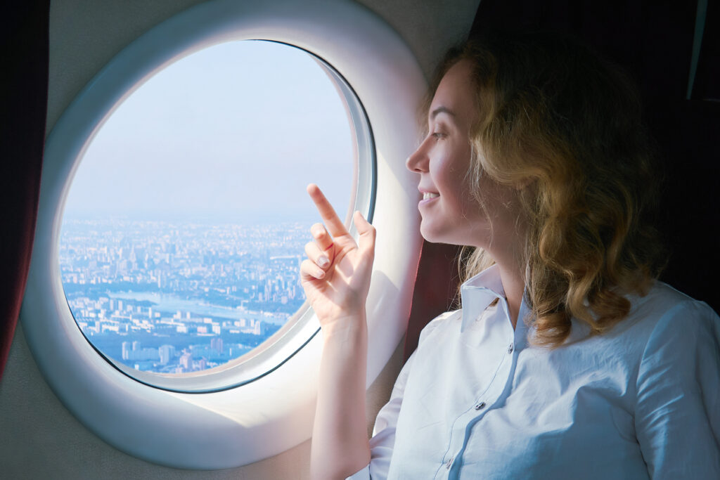 Mulher dentro de um avião olhando a paisagem pela janela, voando pela Air France, e acumulando milhas pela Flying Blue.